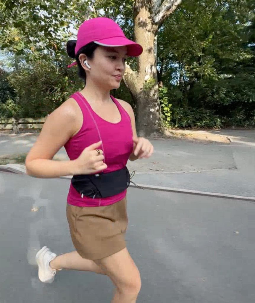 Mika running outside in a pink cap and tank, AirPods in, with a black running belt